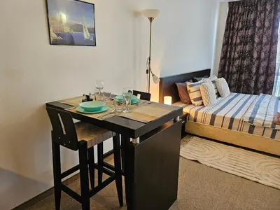 a room with a desk with a bed and a table with wine glasses at Студио за нощувки в Сарафово in Burgas City