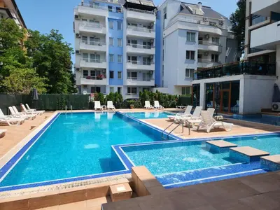 a swimming pool with chairs and a building at Apart VILLA ITTA Sunny Beach in Sunny Beach