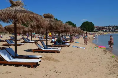 a beach with lounge chairs and straw umbrellas at Flores Garden Pool Side and Sea View Apartment in Chernomorets