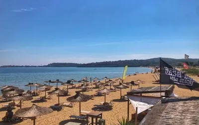 a beach with many umbrellas and chairs and the water at Бунгало Шангри Ла - 2, плаж Градина in Sozopol