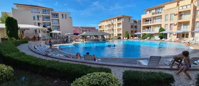 a large swimming pool with people sitting in chairs in front of buildings at Съни Дей ,Слънчев бряг in Burgas City