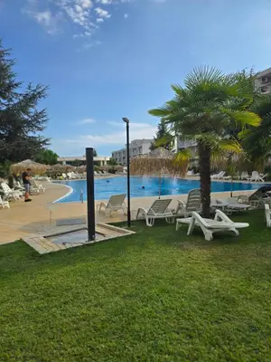 a pool with chairs and a palm tree in a park at Apartament Primavera Atlantis SPA in Burgas City