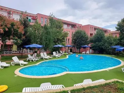 a swimming pool with chairs and umbrellas in front of a building at Double Cherry Apartment in Sunny Beach