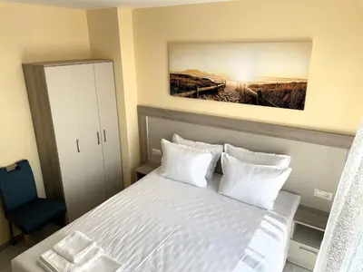a bedroom with a white bed and a blue chair at APART-HOTEL Stamopolu Lux с изглед към морето in Primorsko
