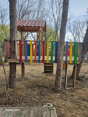 a colorful play structure in a park next to two trees at Бунгало Шангри Ла-3, плаж Градина in Sozopol