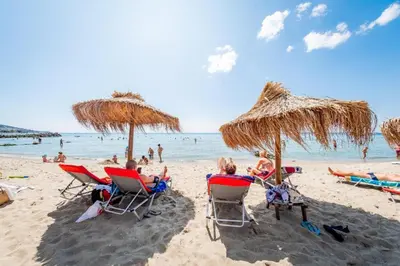 a group of people sitting in lawn chairs under umbrellas on a beach at Panorama Dreams - Prestige Apartments in Sveti Vlas