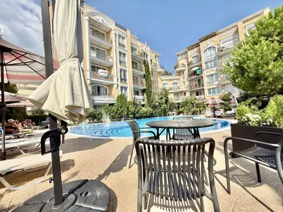 a table and chairs with an umbrella in front of a building at Messembria Palace - Menada Apartments in Sunny Beach