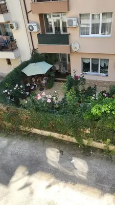 a building with a garden with flowers and an umbrella at Делукс апартамент -Тюркоазен релакс in Pomorie