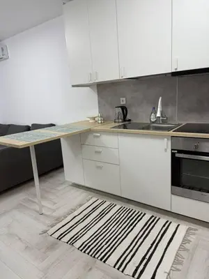 a kitchen with white cabinets and a table and a rug at Sveti Vlas, Rodopi Bay Residence in Sveti Vlas