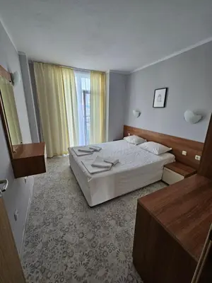 a bedroom with a white bed and a large window at Тристаен просторен апартамент с две отделни спални in Sunny Beach