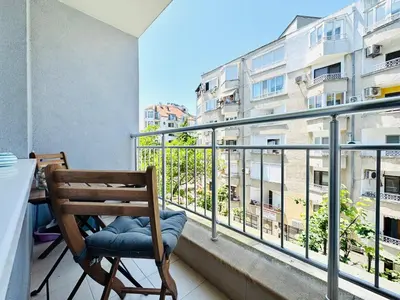 a balcony with a wooden chair and a table and a building at Park suite in Burgas City