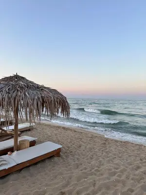 a beach with two beds and a straw umbrella at 2 Zimmerwohnung in Shkorpilovtsi