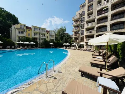 a swimming pool with chairs and umbrellas next to a building at KALIA C2 Two Bedroom Apartment Sunny Beach in Sunny Beach