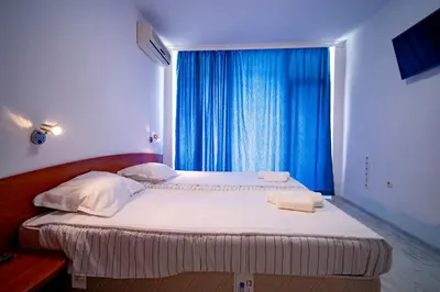 a bedroom with two beds and a window with blue curtains at Harmani Haven 1BD Apartment with Own Parking spot by Flat Manаger in Sozopol