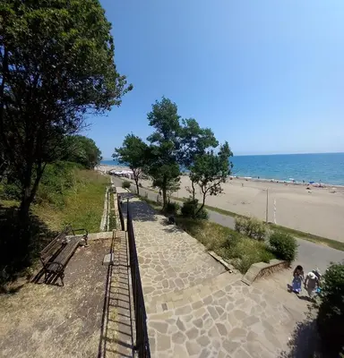 a view of a beach with two people sitting on benches at Студио Слънчева перла in Burgas City