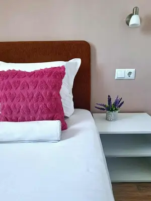 a white bed with a pink pillow and a table at Chance Sarafovo in Burgas City