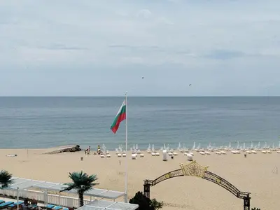 a flag on a beach with chairs and umbrellas at Апартамент в КК 