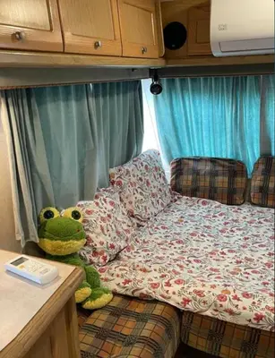 a green frog sitting on a bed in an rv at Яката Каравана in Kiten