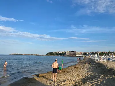 a man standing on a beach with people in the water at ATOS 507 Studio Sunny Beach in Sunny Beach