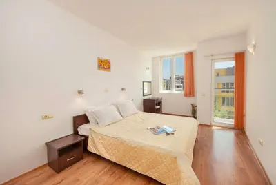 a white bedroom with a bed and a window at Sunny Holiday Apartments in Sunny Beach