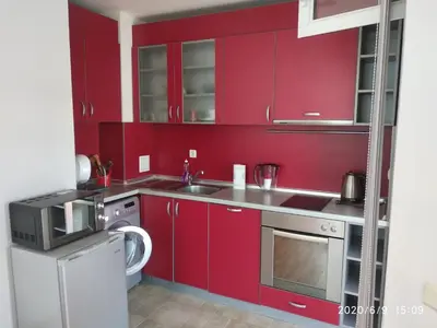 a red kitchen with a sink and a dishwasher at Apartment Stoyanovi in Primorsko