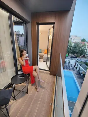 a woman in a red dress sitting on a chair on a balcony at Sunny Bay Sweet Homes Lux Apartment in Sunny Beach