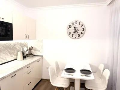 a white kitchen with a table and a clock on the wall at Stylish studio near harbor and luxury beach in Sveti Vlas