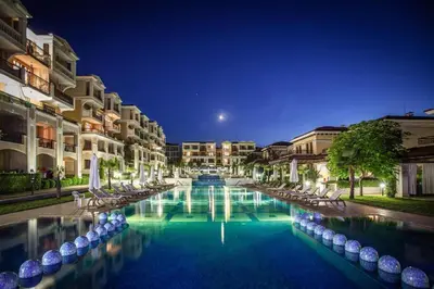 a large swimming pool with chairs and buildings at night at Studio Vanita in Sozopol