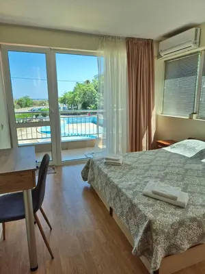 a bedroom with a bed and a desk and a balcony at Първа Линия Лазур Поморие in Pomorie