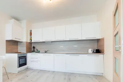 a white kitchen with white cabinets and a wooden floor at АТ apartment - South Bay Beach Residence in Varna City