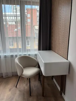 a white desk and a chair in a room with a window at Дизайнерски апартамент in Burgas City