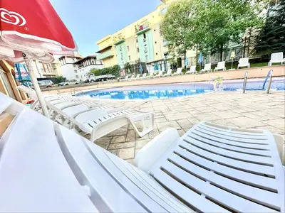 a pool with white lounge chairs and an umbrella at Sunny Sea - Menada Apartments in Sunny Beach