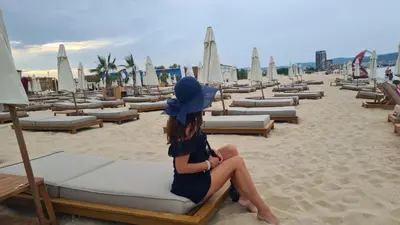 a woman sitting on a chair on the beach at Apartment 16 - Rainbow Holiday Complex in Sunny Beach