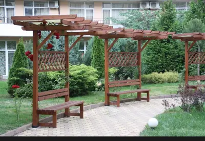 a wooden pergola with two benches in a yard at Уютная студия на Солнечном берегу in Sunny Beach