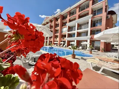 a hotel with red flowers in front of a swimming pool at Carina Beach - Menada Apartments in Sunny Beach