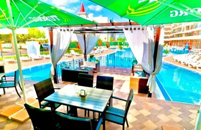 a table and chairs with umbrellas next to a swimming pool at Grand Kamelia Apartments Sunny Beach in Sunny Beach