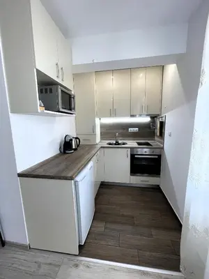 a kitchen with white cabinets and a wooden floor at Velaria Centre Apartment in Burgas City