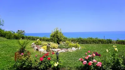 a garden with flowers and the ocean in the background at Апартаменти Бяла Клиф - Byala Cliff Apartments in Byala
