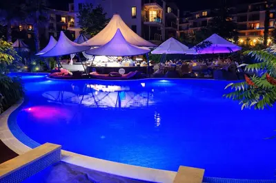 a swimming pool at night with tables and umbrellas at Harmony Suites-4 Private Apartment B544 in Sunny Beach