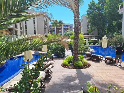 a courtyard with chairs and palm trees next to a pool at 3 Room Apartment with Poolview in Cascadas Resort in Sunny Beach