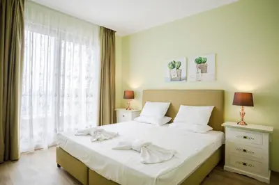 a bedroom with a bed with white sheets and a window at Gardenia Beach Palace Aparthotel in Pomorie