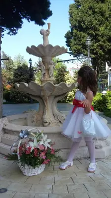 a little girl in a wedding dress standing in front of a fountain at Villa Roma Monna in Nesebar