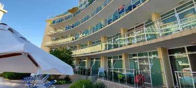 a building with chairs and an umbrella in front of it at Julia Family Apartments in Sunny Beach