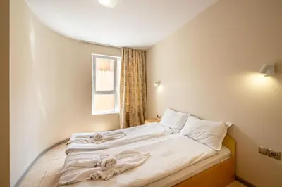 a bedroom with a bed with white sheets and a window at Perla Apartments in Nesebar