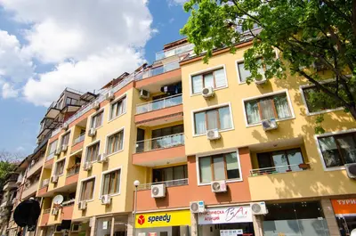 a tall yellow and orange building on a street at Sea Garden Apartment IDM in Varna City
