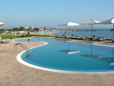 a swimming pool with chairs and umbrellas next to the ocean at Samara Apartment in Lozenets