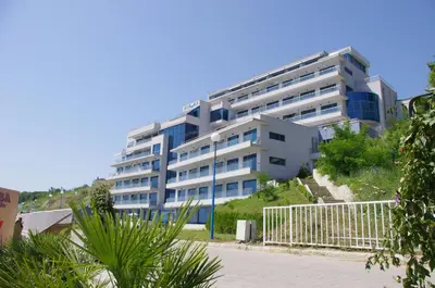 a large white building with blue windows on a hill at Aurora apartments on the beach in Obzor