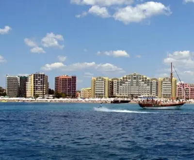 a boat in the water in front of a city at Hotel Shipka Beach in Sunny Beach