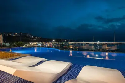 a swimming pool with white lounge chairs at night at Blu Bay Hotel Sozopol in Sozopol