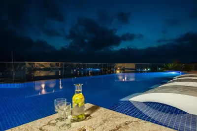 a bottle of wine and glasses on the edge of a swimming pool at night at Blu Bay Hotel Sozopol in Sozopol